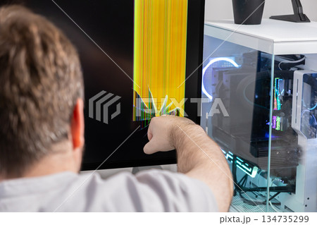 Man pointing at a severely broken computer monitor with colorful vertical lines and cracks, symbolizing technology failure, frustration, or the need for repair 134735299