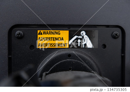 Close-up of yellow warning label with WARNING ADVERTENCIA AVERTISSEMENT text and graphic of person lifting, indicating important safety information for industrial machinery operation 134735305