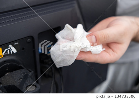 Person's hand holds a dirty cleaning cloth wiping dust from a computer monitor, promoting workspace hygiene and essential electronic device care 134735306
