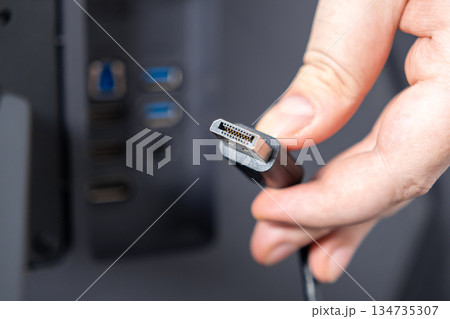 Hand holding a DisplayPort cable connector, highlighting its detailed pins, signifying essential high-resolution video connectivity for computer system 134735307