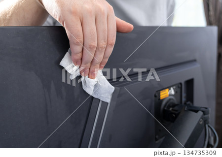 Hand diligently cleaning a dusty black computer monitor with a white wet wipe, ensuring hygiene and proper maintenance in a modern digital workspace Hand diligently cleaning a dusty black computer monitor with a white wet wipe, ensuring hygiene and proper maintenance in a modern digital workspace 134735309