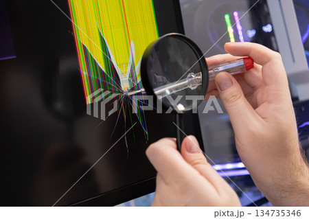 Hands inspecting a severely cracked computer monitor screen with a magnifying glass, highlighting urgent hardware repair and technology problems 134735346