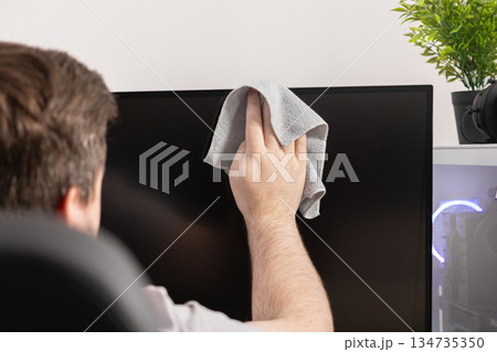 Hand carefully wiping a computer monitor screen with a grey microfiber cloth, highlighting desktop hygiene and essential tech maintenance in a modern home office 134735350