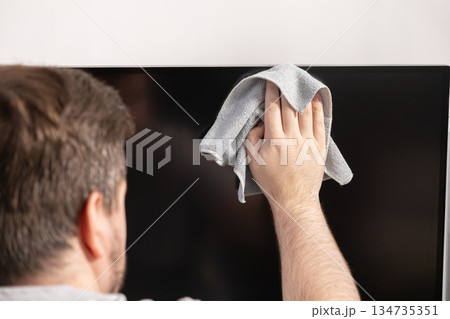 Person's hand diligently wiping a large, dark television screen with soft grey microfiber cloth, promoting home hygiene and electronic device care Person's hand diligently wiping a large, dark television screen with soft grey microfiber cloth, promoting home hygiene and electronic device care 134735351
