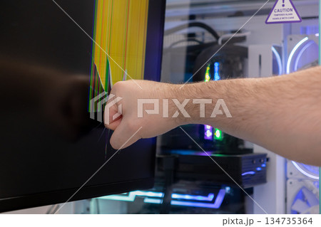 Aggressive persons fisted hand violently hits a gaming monitor, shattering the screen into a vibrant display of broken pixels, portraying intense digital frustration and tech rage Aggressive persons fisted hand violently hits a gaming monitor, shattering the screen into a vibrant display of broken pixels, portraying intense digital frustration and tech rage 134735364