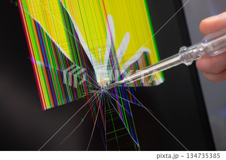 Hand pointing a clear screwdriver at a severely cracked electronic screen with vibrant pixel lines, illustrating digital device damage and repair necessity Hand pointing a clear screwdriver at a severely cracked electronic screen with vibrant pixel lines, illustrating digital device damage and repair necessity 134735385