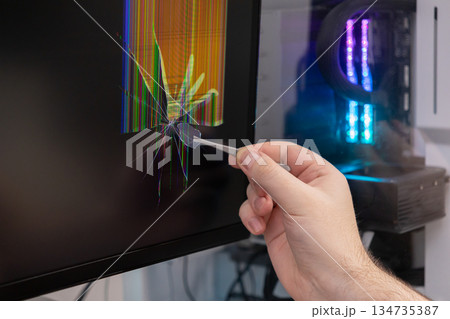 A hand uses delicate tweezers to extract a glass shard from a severely cracked computer monitor, symbolizing technology damage and repair challenges 134735387