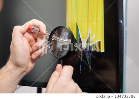 A person inspects a broken computer monitor with a magnifying glass, revealing a cracked screen and yellow glitch lines, indicating electronic repair A person inspects a broken computer monitor with a magnifying glass, revealing a cracked screen and yellow glitch lines, indicating electronic repair 134735388