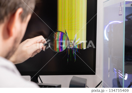Man examining a broken computer monitor with a magnifying glass, showing screen damage and the need for technical repair or IT problem troubleshooting Man examining a broken computer monitor with a magnifying glass, showing screen damage and the need for technical repair or IT problem troubleshooting 134735409