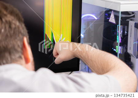 A furious person's fist violently smashes a computer monitor, creating a severely cracked screen with yellow and colorful lines, symbolizing intense frustration and tech failure 134735421