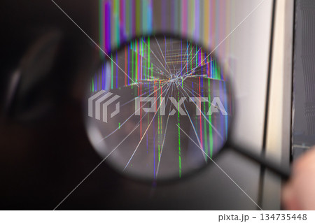 Magnifying glass examining a severely cracked digital screen with vibrant vertical lines, illustrating electronic device damage, malfunction, and inspection 134735448