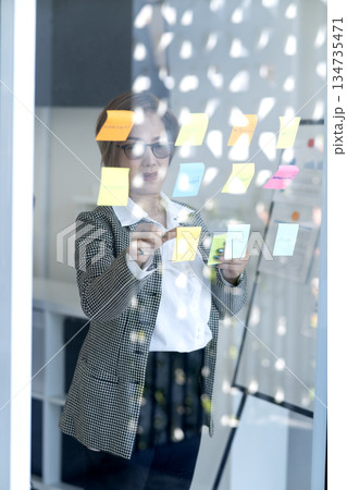Senior business woman is looking at and writing messages on sticky notes Senior business woman is looking at and writing messages on sticky notes 134735471