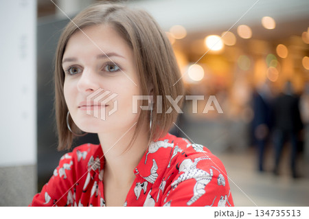 Young women in red shirt looks away on the background of a shopping center Young women in red shirt looks away on the background of a shopping center 134735513