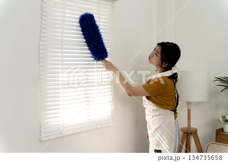 Young woman is using a duster to clean the windows of the house 134735658