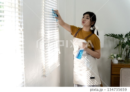Young woman is using a duster to clean the windows of the house 134735659