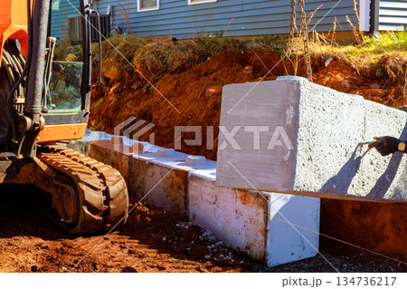 Construction excavator puts large concrete blocks in trench for retaining walls 134736217