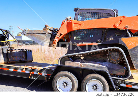Loader with attachments is positioned on trailer by construction site along road Loader with attachments is positioned on trailer by construction site along road 134736220