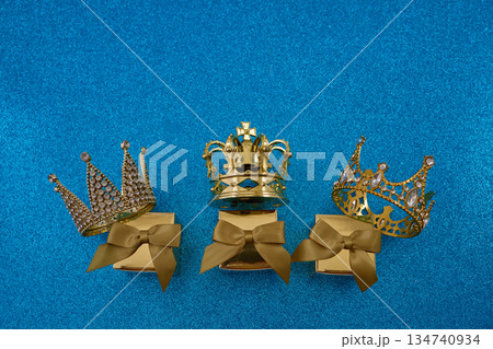 Three gold crowns on gift boxes on blue glittering background Three gold crowns on gift boxes on blue glittering background 134740934