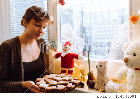 young woman holding gingerbread cookies on a wooden round board 134741001