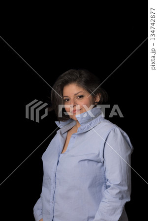 A woman is wearing a blue shirt and standing in front of a black background A woman is wearing a blue shirt and standing in front of a black background 134742877
