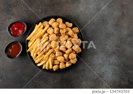 Crispy chicken popcorn and french fries with ketchup, sweet sauce on gray background. Fast food combo. Top view. Crispy chicken popcorn and french fries with ketchup, sweet sauce on gray background. Fast food combo. Top view. 134743703