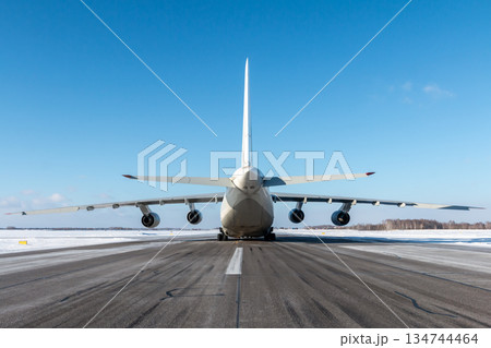 Large heavy transport aircraft on the runway of winter airport. Rear view Large heavy transport aircraft on the runway of winter airport. Rear view 134744464