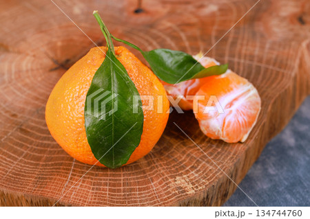 An organic tangerine on wooden board with leaf with half of orange fruit inside. An organic tangerine on wooden board with leaf with half of orange fruit inside. 134744760