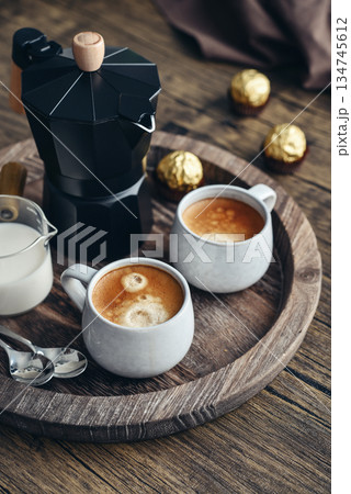 Black moka pot coffee maker with wooden handle and  two cups  of coffee 134745612