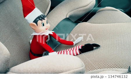 Close up of a festive Christmas elf doll placed on a modern car seat inside vehicle interior. Seasonal decoration concept combining holiday tradition family travel and everyday transportation Close up of a festive Christmas elf doll placed on a modern car seat inside vehicle interior. Seasonal decoration concept combining holiday tradition family travel and everyday transportation 134746132