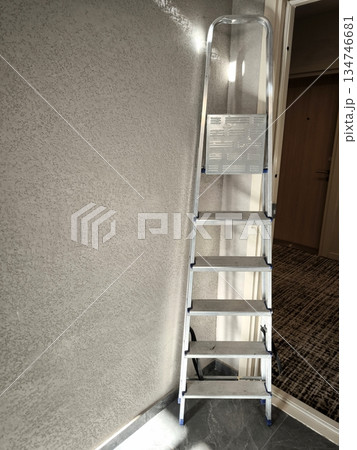An aluminum stepladder leaning against a textured wall indoors 134746681