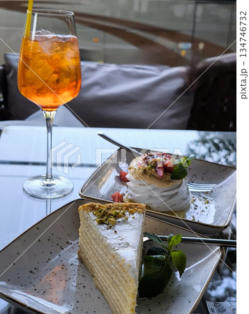Summer fun: an orange cocktail and two exquisite desserts on a glass table 134746732