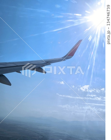 Airplane wing, bright sun and mountains, view from the window Airplane wing, bright sun and mountains, view from the window 134746739