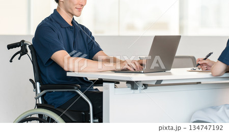 オフィスでデスクワークする車椅子に乗る男性スタッフ 134747192