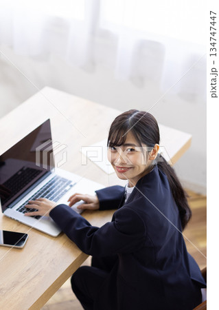 パソコンで作業をしながらカメラ目線で微笑む若いビジネスウーマン 134747447