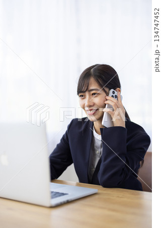 パソコンで作業しながらスマートフォンで通話するスーツ姿の女性 パソコンで作業しながらスマートフォンで通話するスーツ姿の女性 134747452