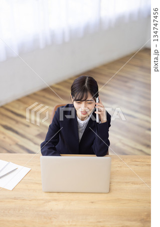 パソコンで作業しながらスマートフォンで通話するスーツ姿の女性 134747456