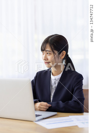 パソコン作業の合間に窓の外を見るスーツを着た若い女性 134747712