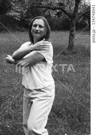 Happy middle-aged woman enjoying nature and embracing herself in spring field. Concept of self-love, female health, emotional balance, mindfulness, and positive aging 134748041