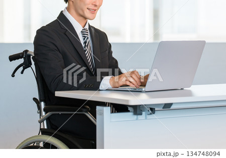 オフィスでデスクワークする車椅子に乗るスーツ姿のビジネスマン男性 134748094