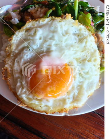 Fried egg sunny side up breakfast on white plate, crispy edge, runny yolk, closeup on rustic wooden table 134748275