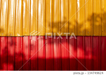 Vibrant metal wall with red and yellow panels and tree shadow creating dynamic texture for modern architectural backgrounds 134749624