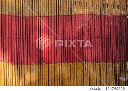 Red and Yellow Bamboo Fence with Sunlight Streaks Creating Visual Texture, a Rustic and Abstract Background for Natural Design Elements 134749626
