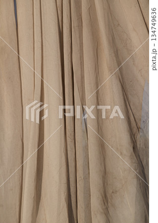 Beige fabric curtain with soft folds and subtle shadows for background texture or drapery design element 134749636
