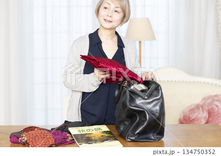 リビングで旅行の荷造りをするシニア女性 リビングで旅行の荷造りをするシニア女性 134750352
