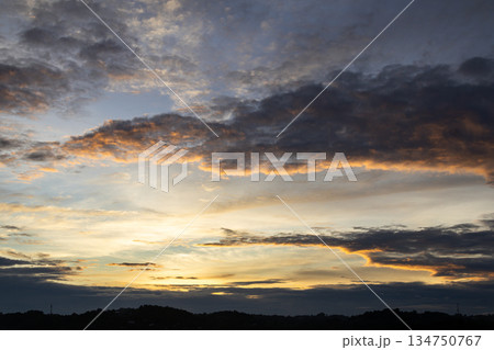 Dramatic sunset sky with dark clouds and golden light casting over silhouette horizon, creating peaceful nature concept Dramatic sunset sky with dark clouds and golden light casting over silhouette horizon, creating peaceful nature concept 134750767