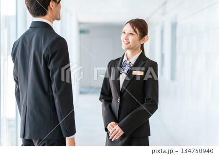 オフィスの廊下で会話するスーツ姿の若いアジア人ビジネスマン男女 オフィスの廊下で会話するスーツ姿の若いアジア人ビジネスマン男女 134750940