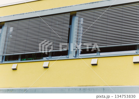 The innovative and modern design of architectural windows incorporates elegant blinds and showcases a vibrant yellow facade, creating a striking appearance that enhances urban aesthetics The innovative and modern design of architectural windows incorporates elegant blinds and showcases a vibrant yellow facade, creating a striking appearance that enhances urban aesthetics 134753830