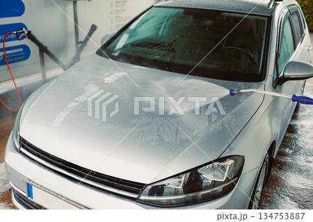 A Clean Start A shiny silver car is being meticulously washed at a selfservice car wash station, utilizing a powerful highpressure water jet to remove dirt and grime effectively from its surface 134753887