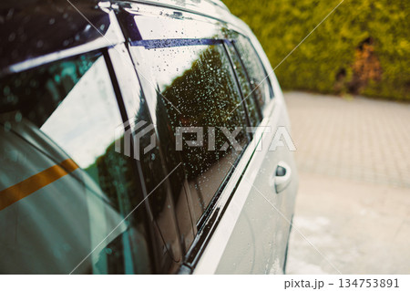 A closeup view of rain droplets perched delicately on a car window captures the beauty of reflected greenery alongside the charming cobblestone pavement below, illustrating a serene urban setting A closeup view of rain droplets perched delicately on a car window captures the beauty of reflected greenery alongside the charming cobblestone pavement below, illustrating a serene urban setting 134753891