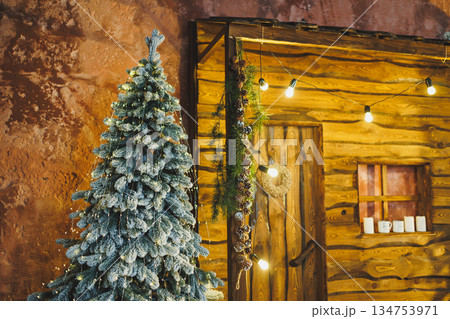 Imagine a cozy Christmas cabin in a snowy landscape, with a frosted tree, sparkling lights, and decorations, creating an inviting atmosphere for warm festive celebrations and joyful gatherings 134753971